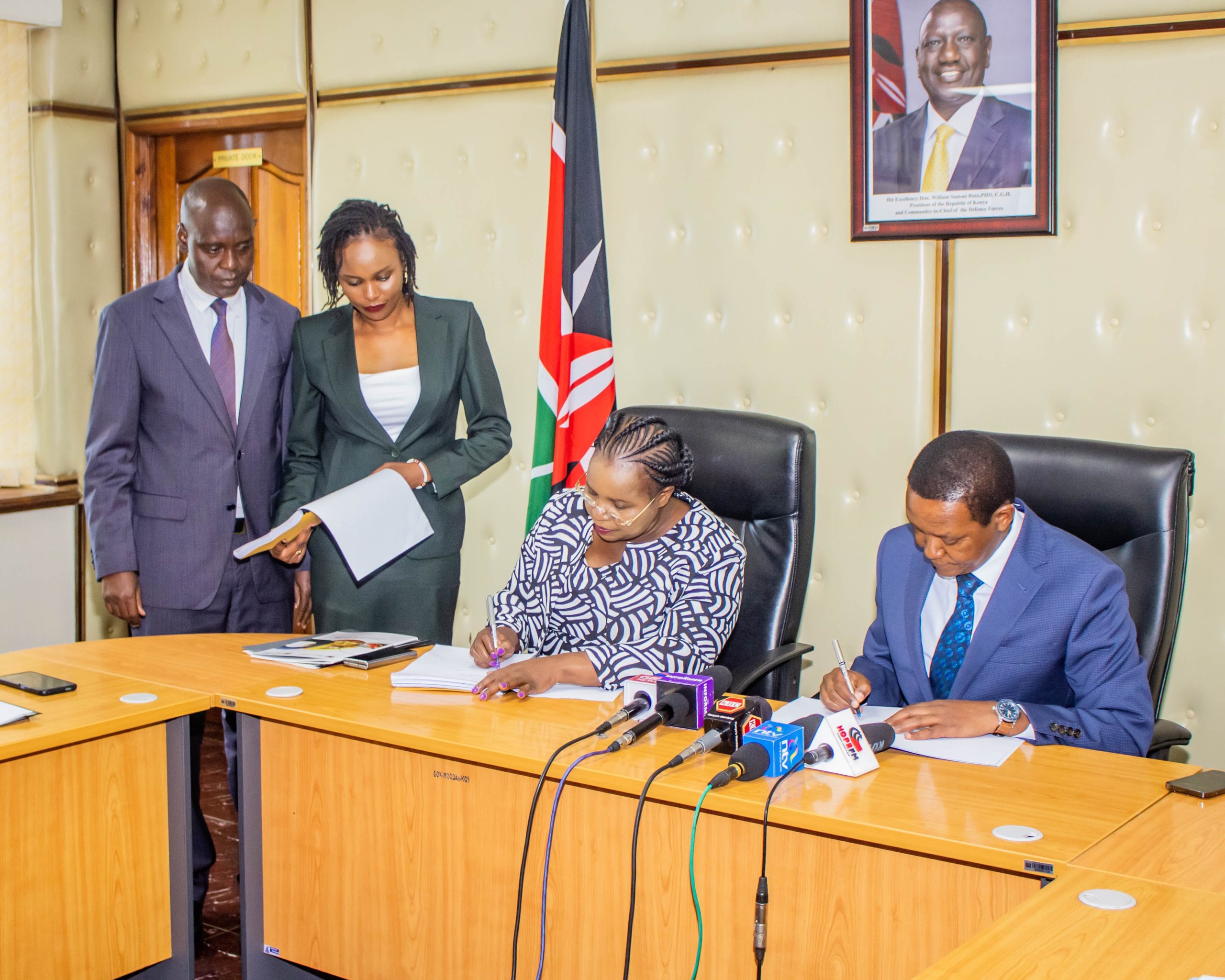 Outgoing Cabinet Secretary (CS) for Tourism and Wildlife Peninah Malonza (Seated Left and the in-coming CS, Dr Alfred Mutua (seated right) sign handing over-taking over notes following some Cabinet re-assignments. Looking on are Principal Secretaries (PS), John Ololtuaa (standing left) and Ms Silvia Museiya (right) for Tourism and Wildlife respectively.
